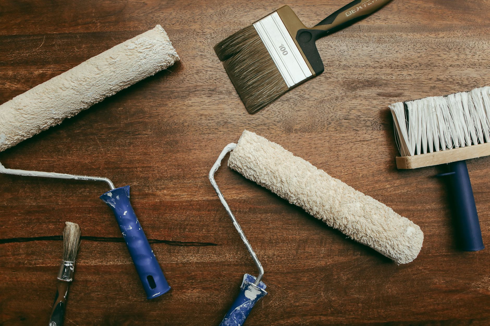 Top view of various painting tools including rollers and brushes laid out on a wooden surface in Pasadena, CA